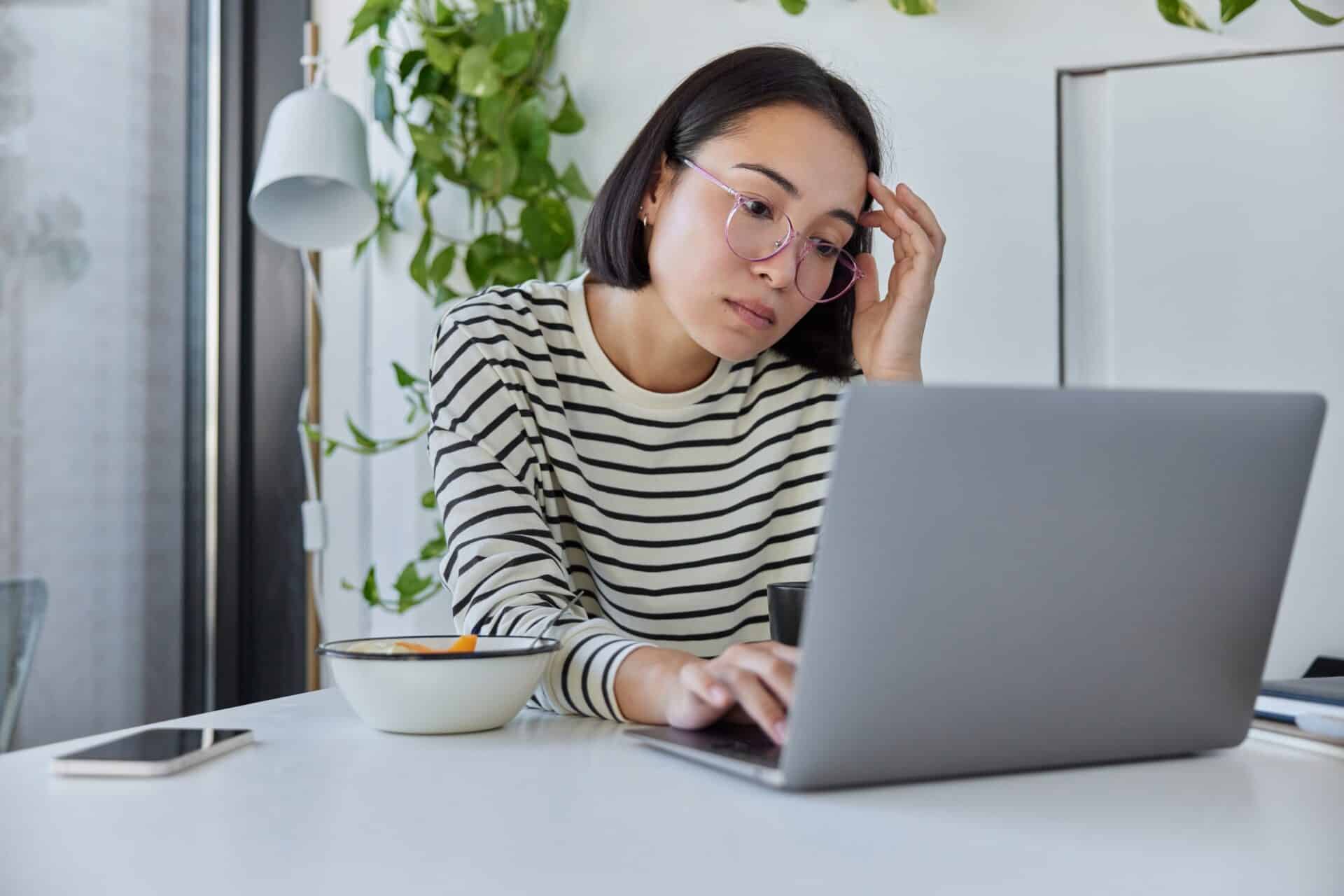 Serious female freelancer with eastern appearance keeps digital nomad lifestyle shares media and mul