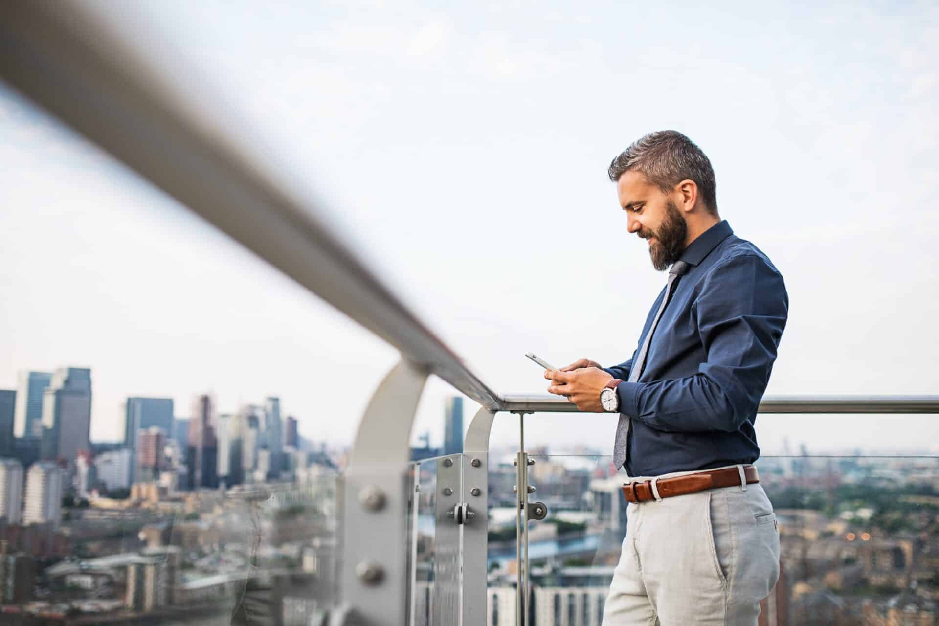 A portrait of businessman with smartphone standing against London view panorama.