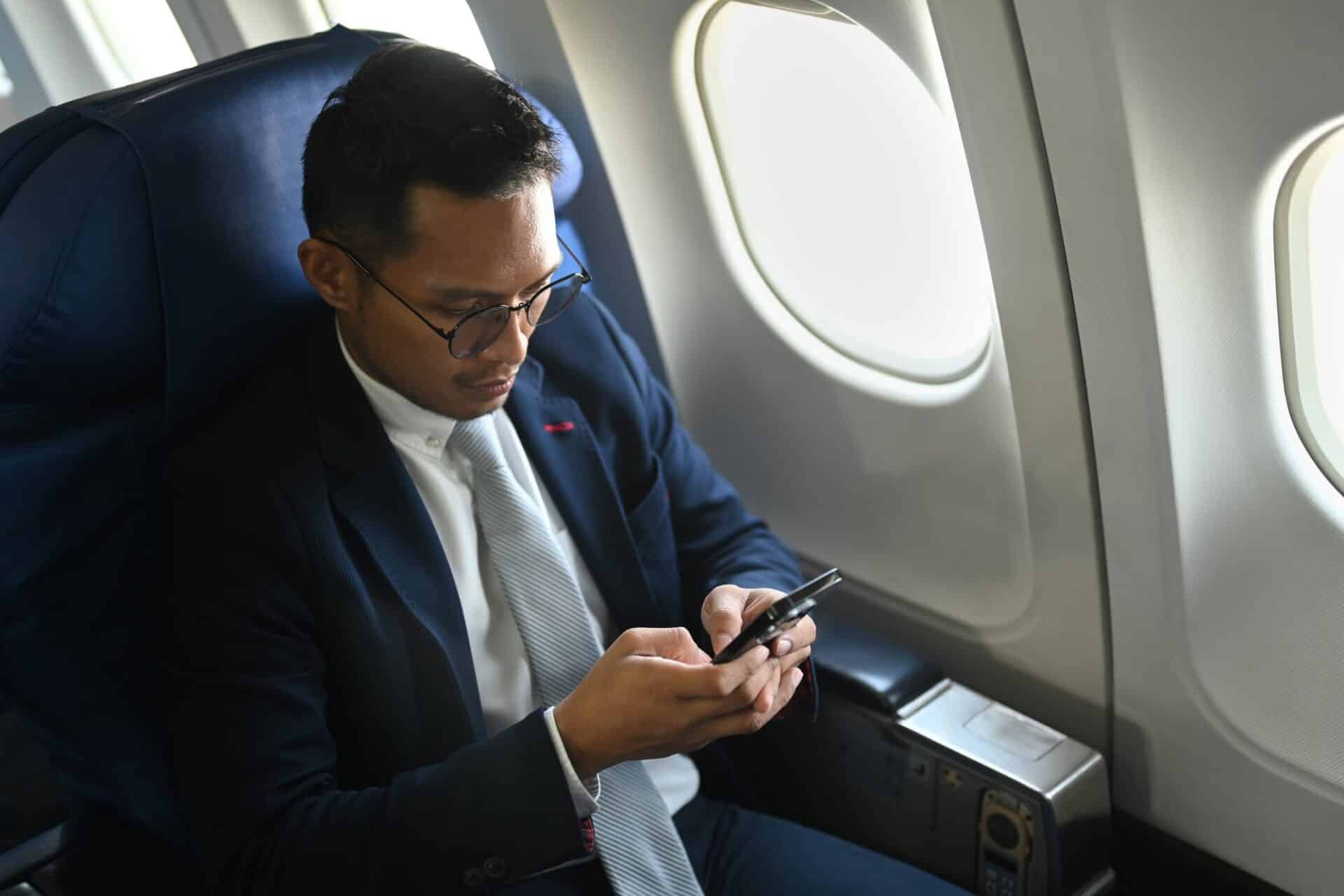 Confident businessman checking news on smart phone during flight.