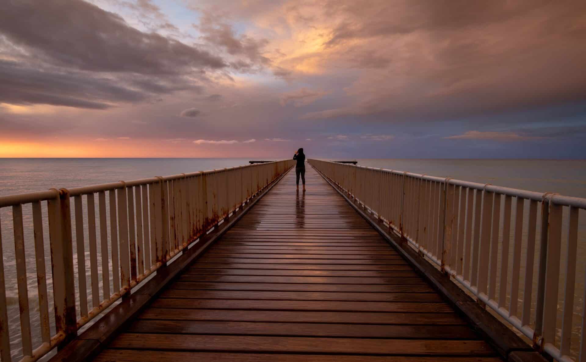 Person standing alone on a pier enjoying dramatic sunset at the sea. Exploring nature