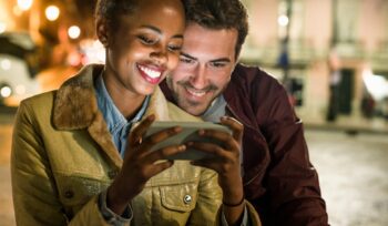 Portrait of happy young couple looking together at smartphone by night, Lisbon, Portugal
