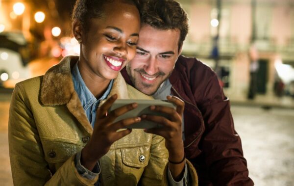 Portrait of happy young couple looking together at smartphone by night, Lisbon, Portugal