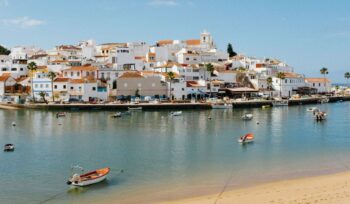 beach with boats in the water and houses on a hill Algarve, Portugal